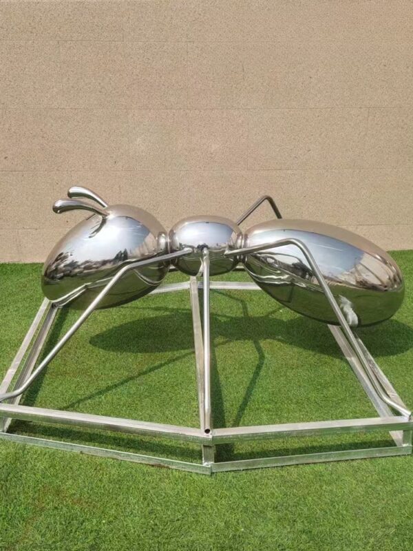 large metallic ant sculpture on a grassy surface