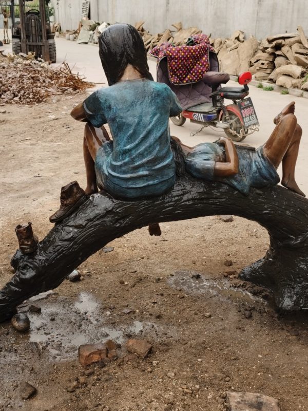 two children sitting on a curved log sculpture