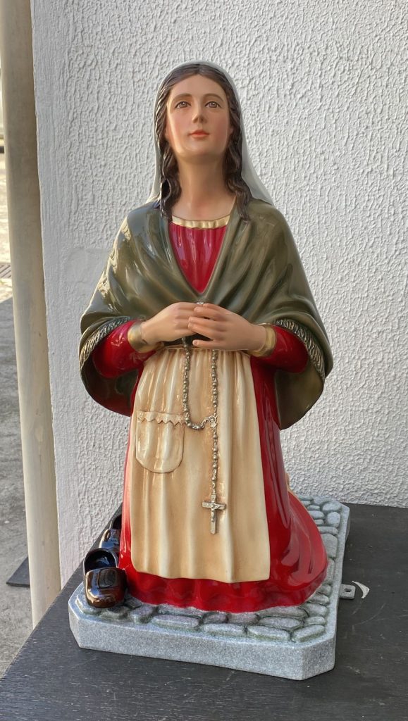 figurative sculpture of a woman in traditional attire holding a rosary